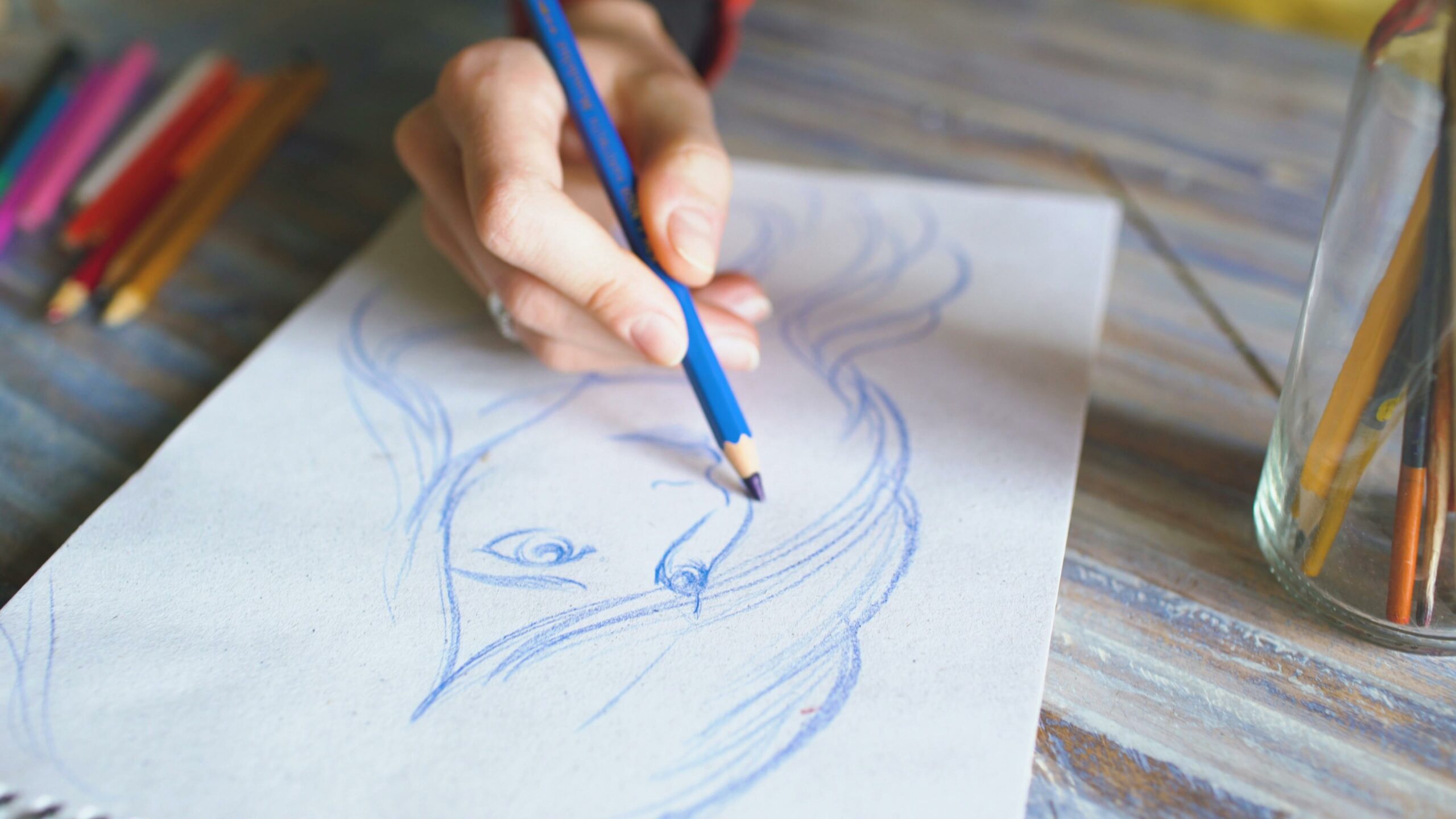 L'école d'Art's Close-up of a hand drawing a portrait using color pencils on paper.